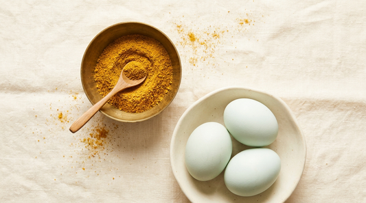 A brass bowl of fine golden salted egg seasoning powder with a wooden spoon, beside whole duck eggs on warm cream linen.
