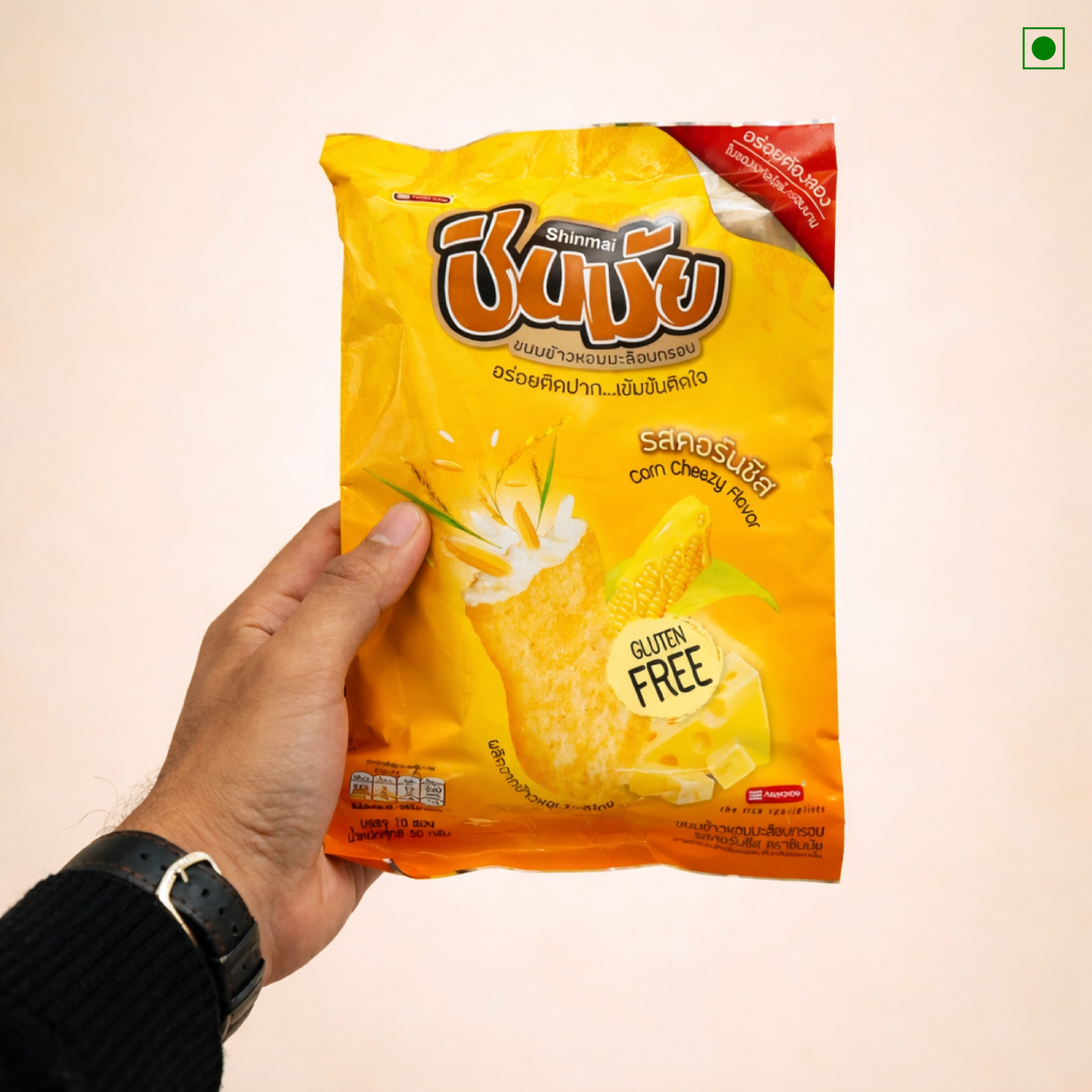 Hand holding a yellow snack packet with branding on a beige background