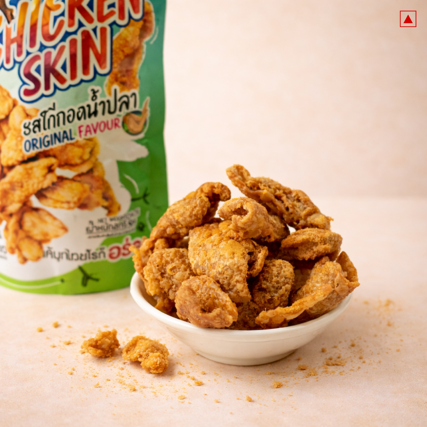 Bowl of fried chicken skin next to a packaging box on a beige background