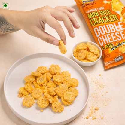 Mini rice crackers with double cheese flavor on a plate and in a bowl, with a hand picking up a cracker.