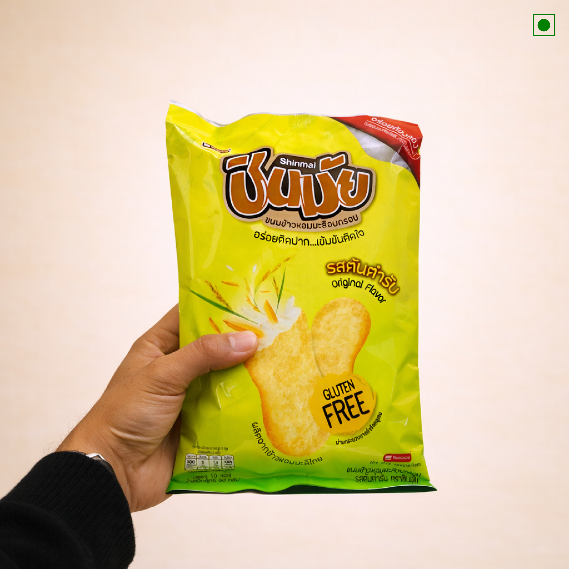 Hand holding a green packet of Shinmai brand gluten-free snacks against a beige background