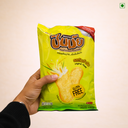 Hand holding a green packet of Shinmai brand gluten-free snacks against a beige background