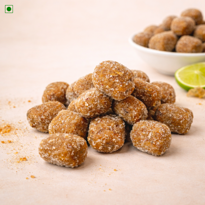 Pile of brown sugar-coated tamarind candy on a light surface with a bowl in the background.