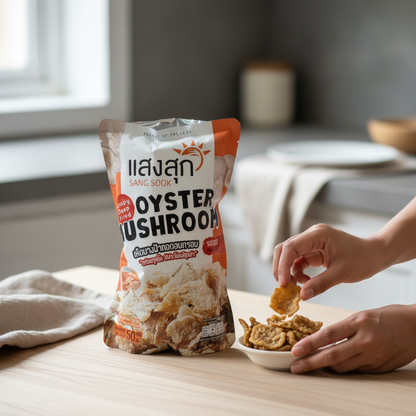 Person dipping oyster mushroom snack into a bowl with a package of Sang Sook Oyster Mushroom on a table.